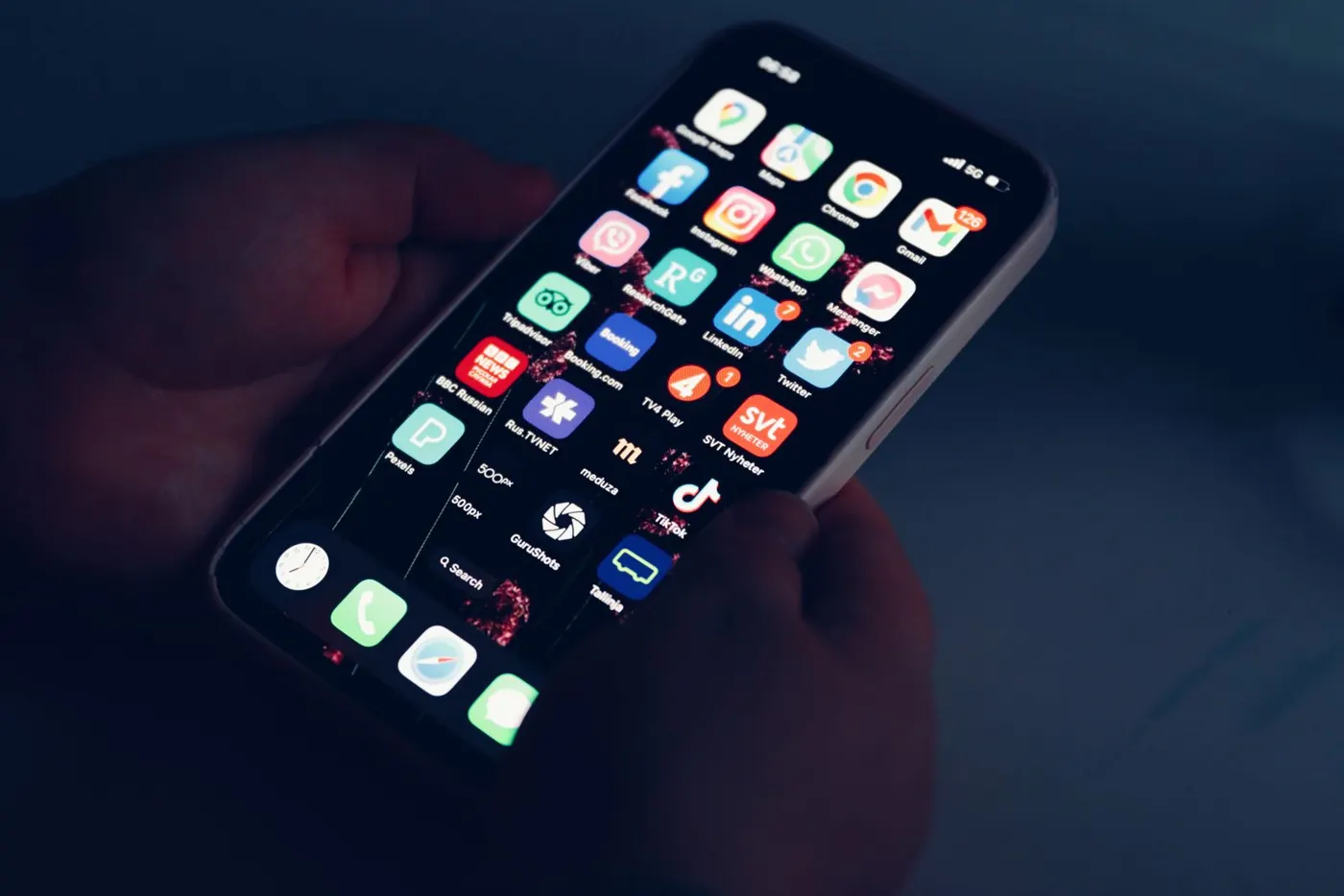 Hands holding a smartphone with app icons in the dark