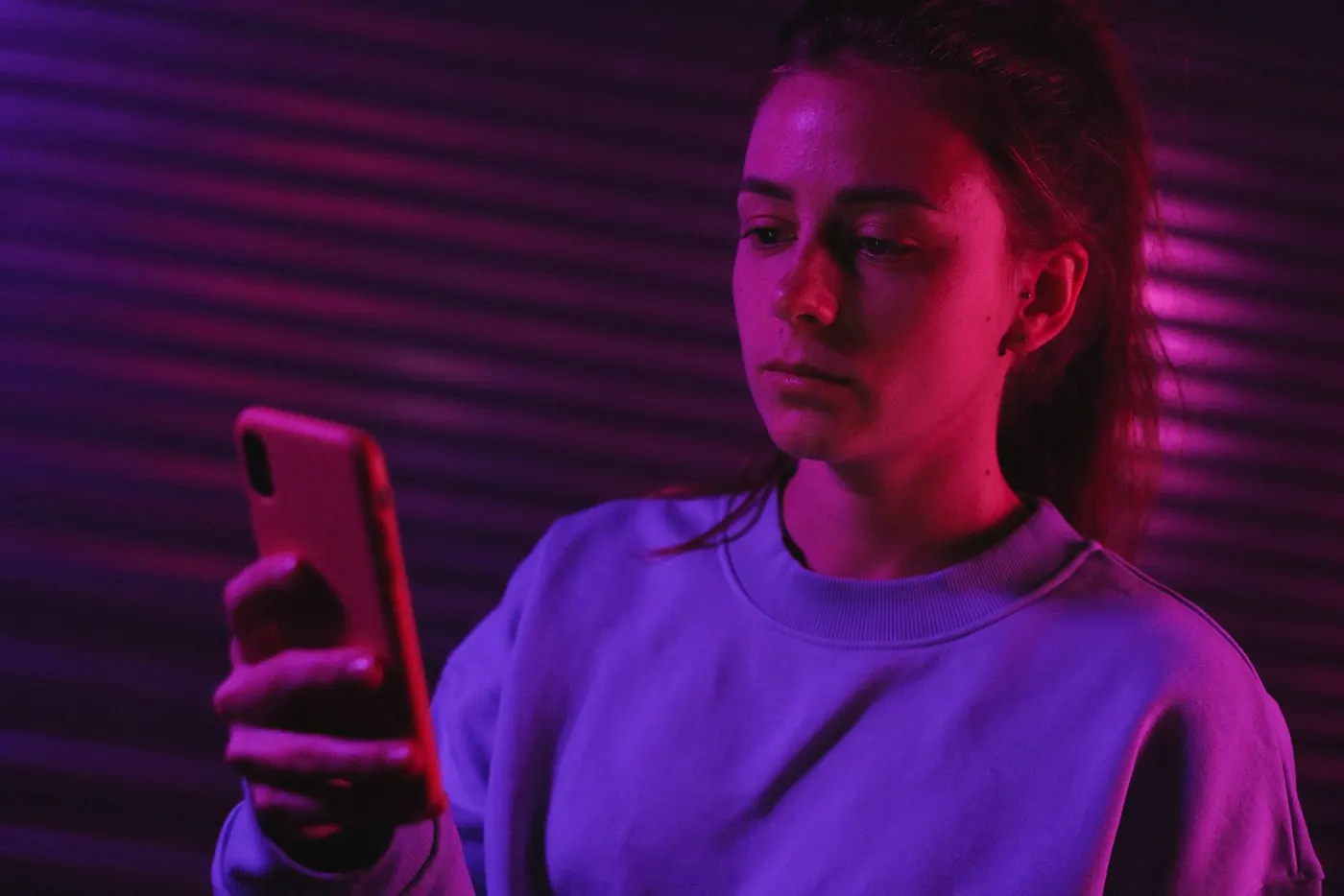 A young woman scrolling on her phone in neon light